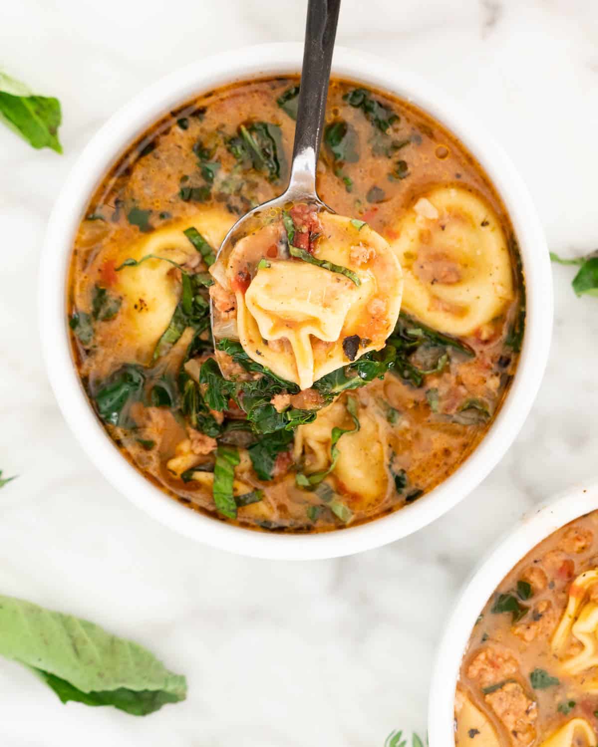 overhead of a bowl of tortellini soup with a spoon holding up a piece of pasta